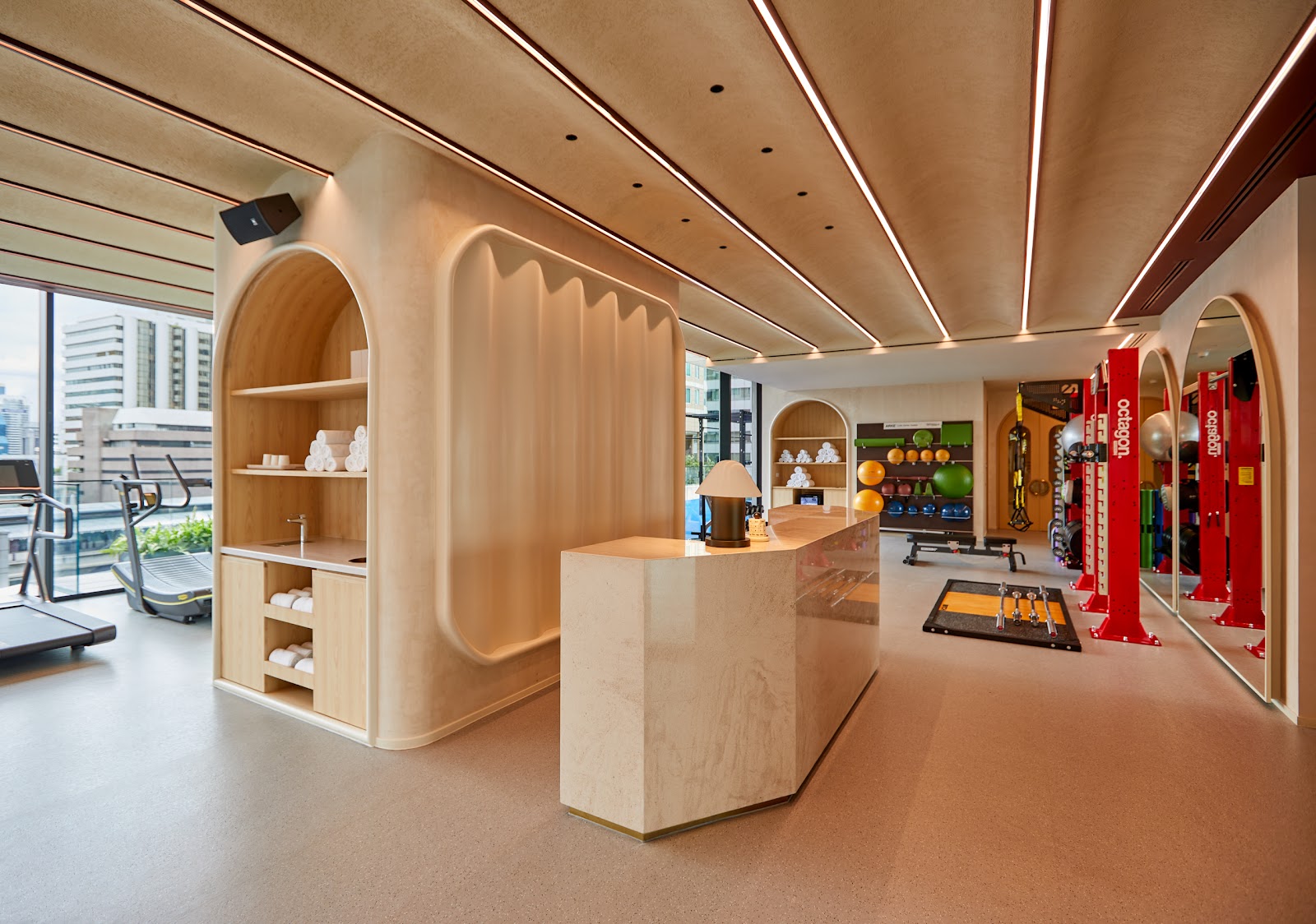Gym reception with arched wooden shelving, towels and exercise equipment beyond