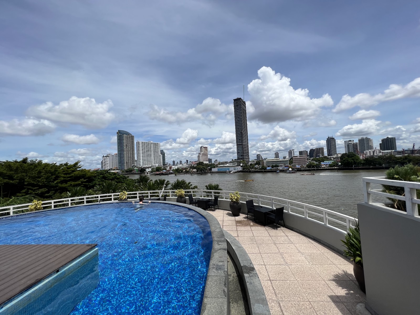 Curved outdoor pool edge overlooking the Chao Phraya River and the skyline on a sunny day