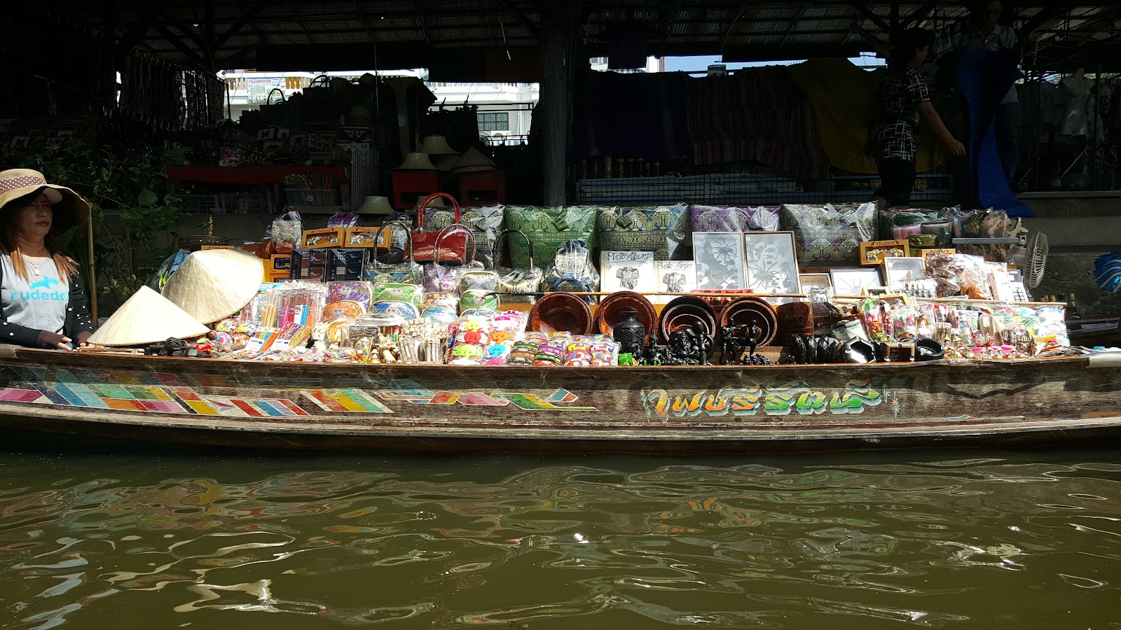 A vendor boat piled with goods moored beside a covered canal-side stall at Damnoen Saduak