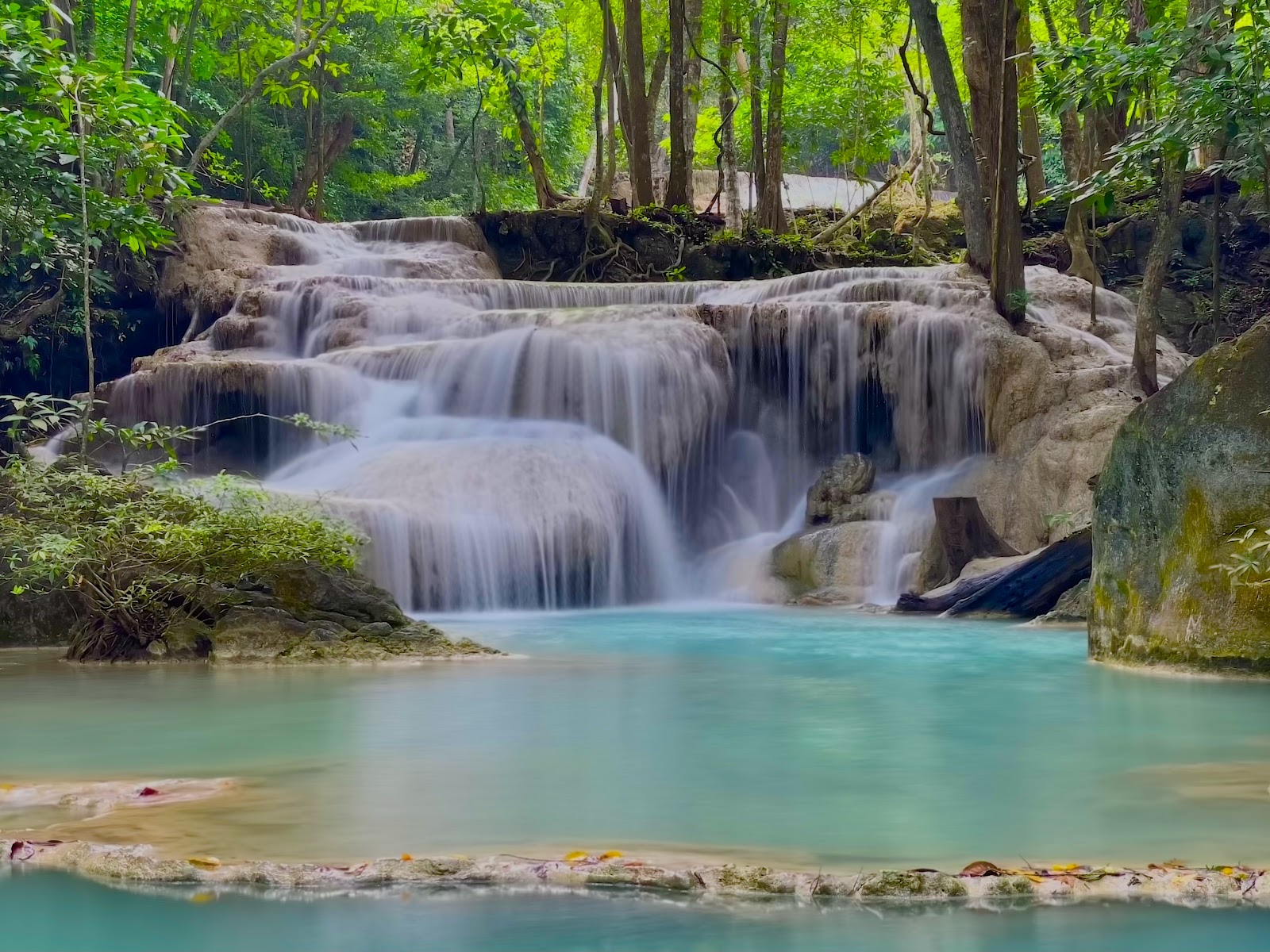 Water spilling over limestone ledges into a turquoise pool at Erawan waterfall