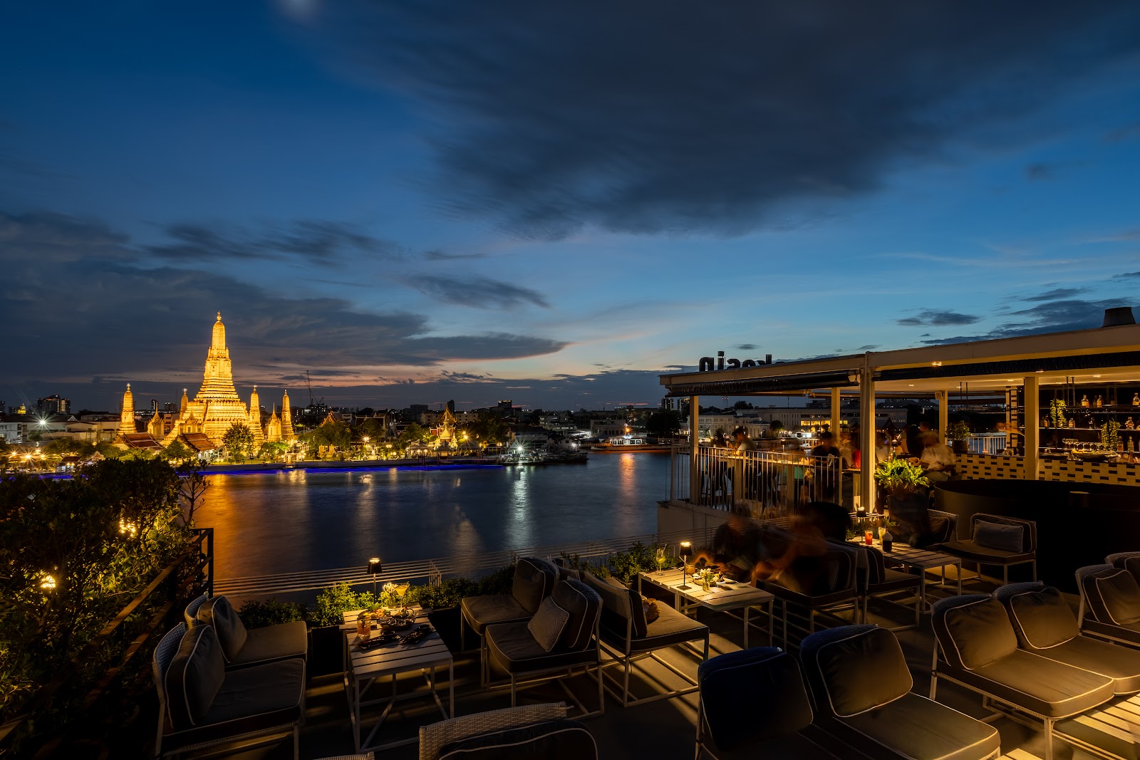 Rooftop terrace of Sala Rattanakosin at dusk with Wat Arun lit across the river