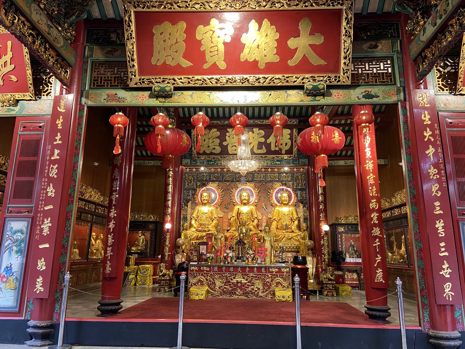 Gilded Buddha images behind red lanterns and pillars in the main hall of Wat Mangkon Kamalawat