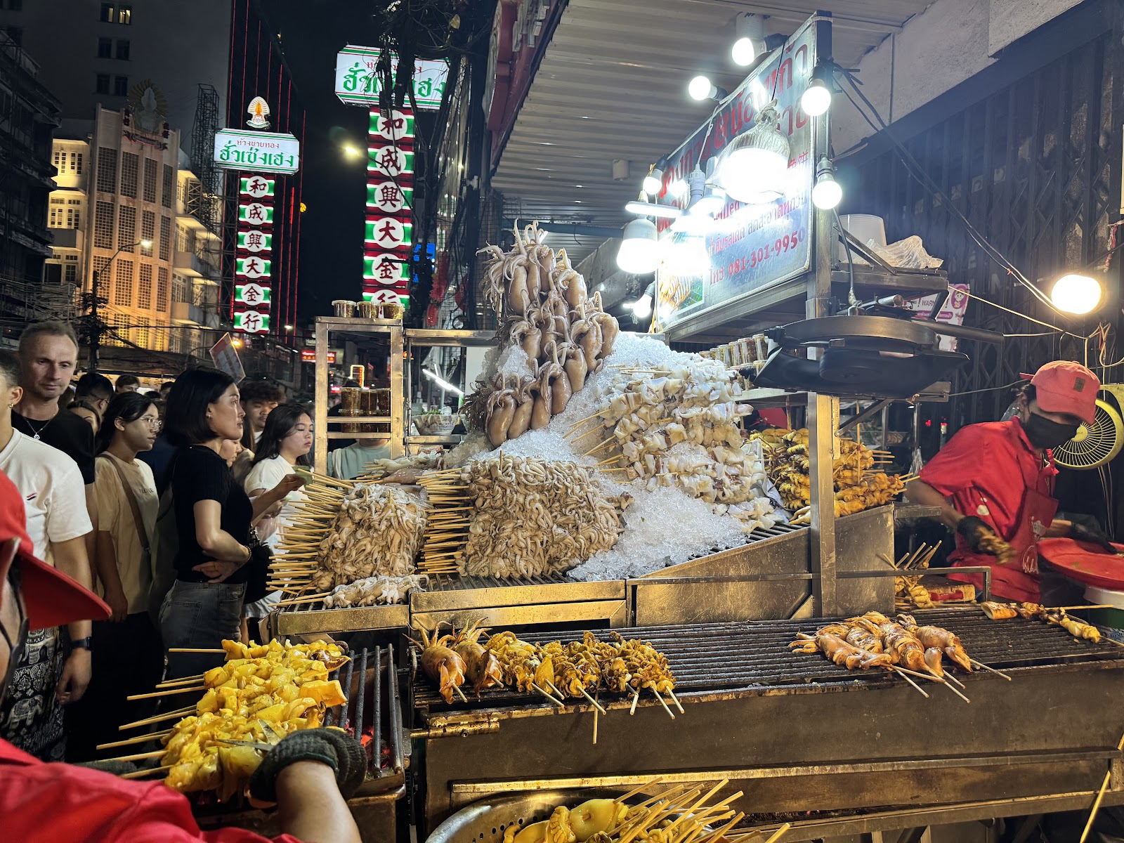 A street food stall grilling seafood under neon signs on Yaowarat Road at night