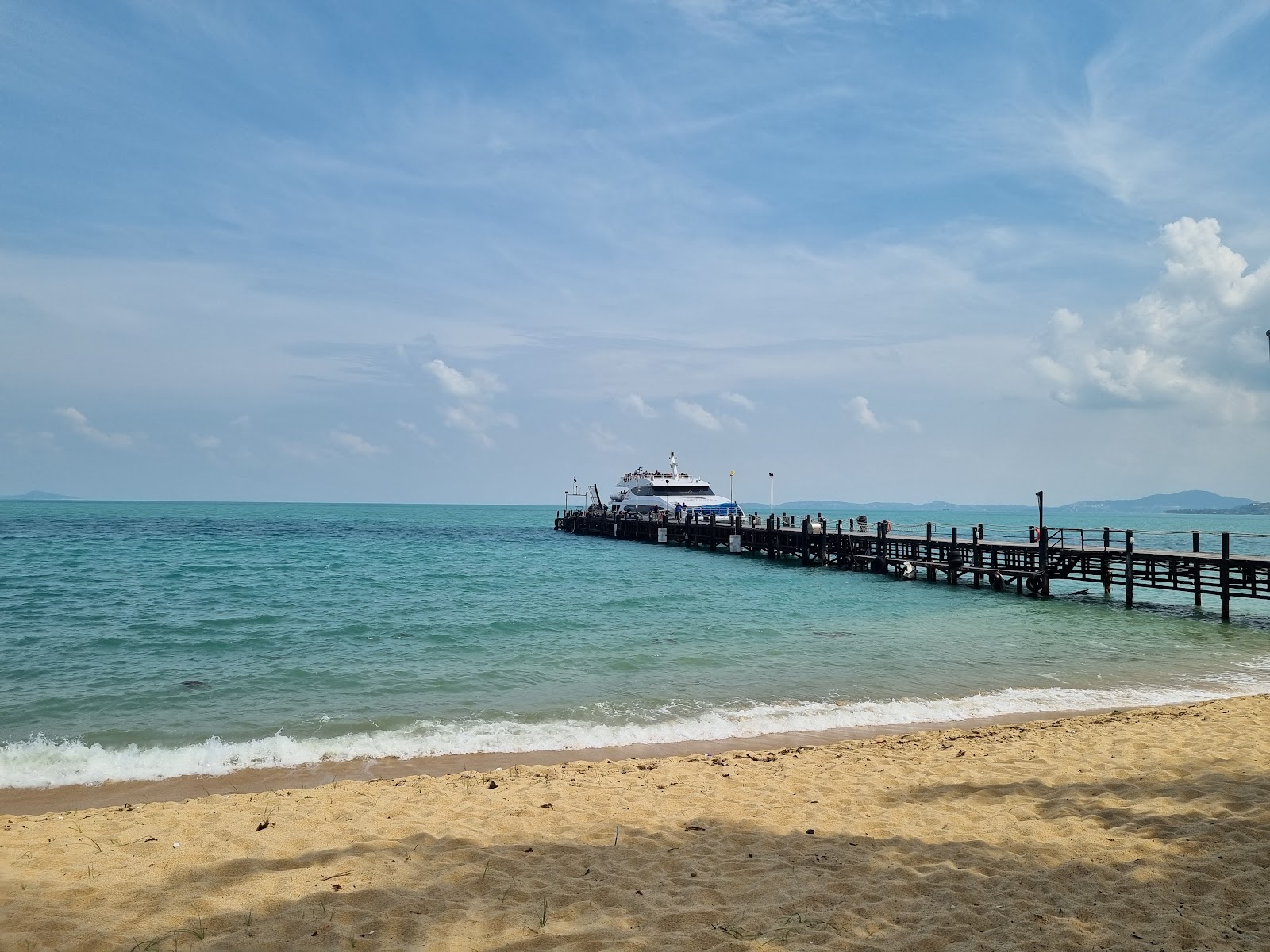 A long wooden pier running out to sea from a sandy beach at Pralarn Pier, Koh Samui