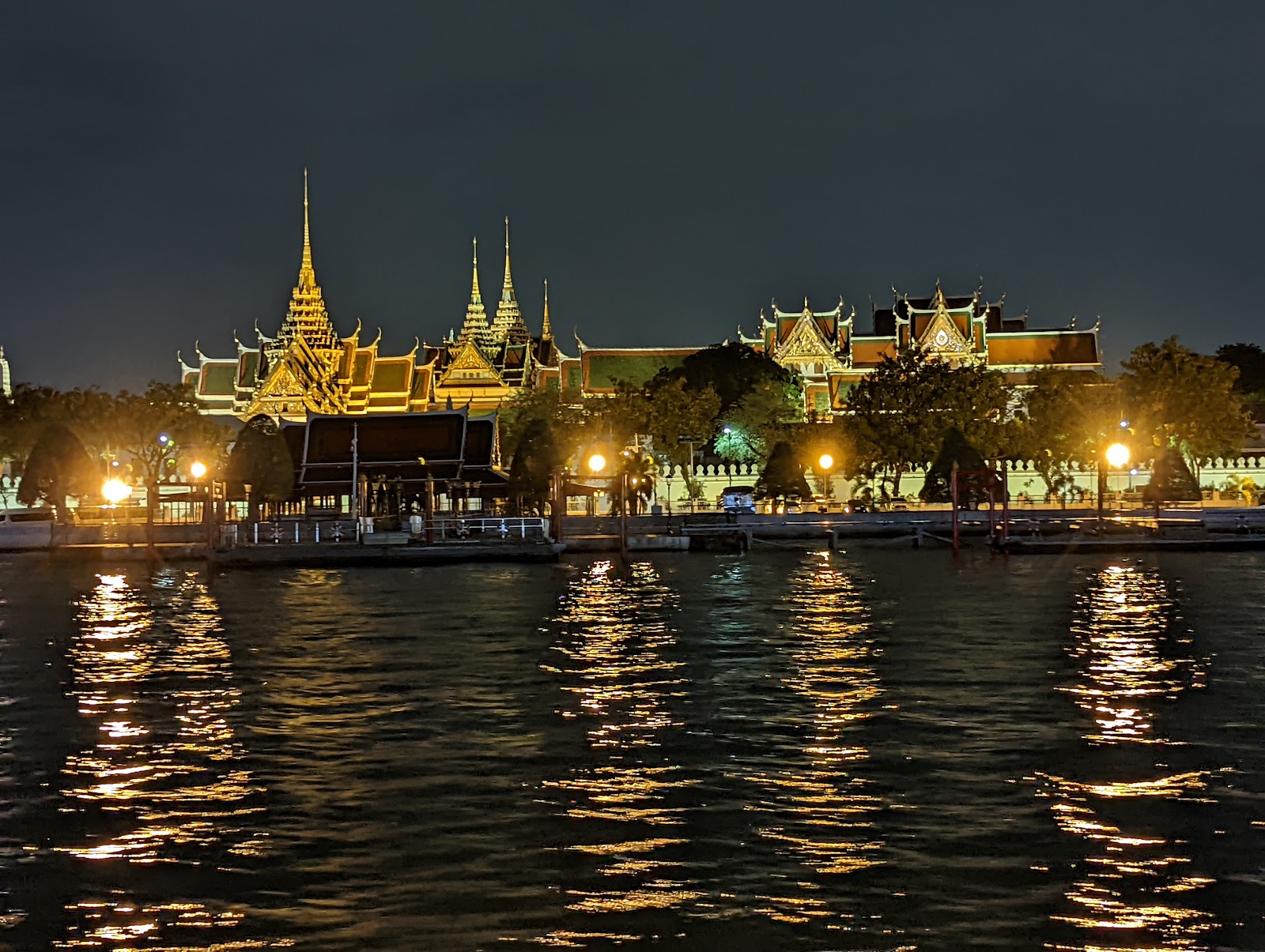 The Grand Palace and its gold spires lit up at night across the dark water of the Chao Phraya River