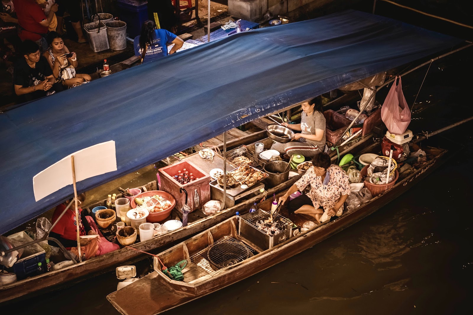 A wooden vendor boat loaded with food and cooking equipment on the canal at Amphawa Floating Market