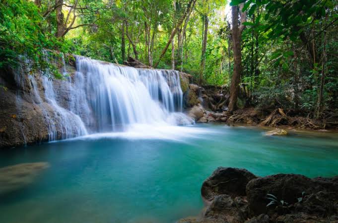 One of the lower tiers of Erawan Falls with a small waterfall above a turquoise pool surrounded by forest
