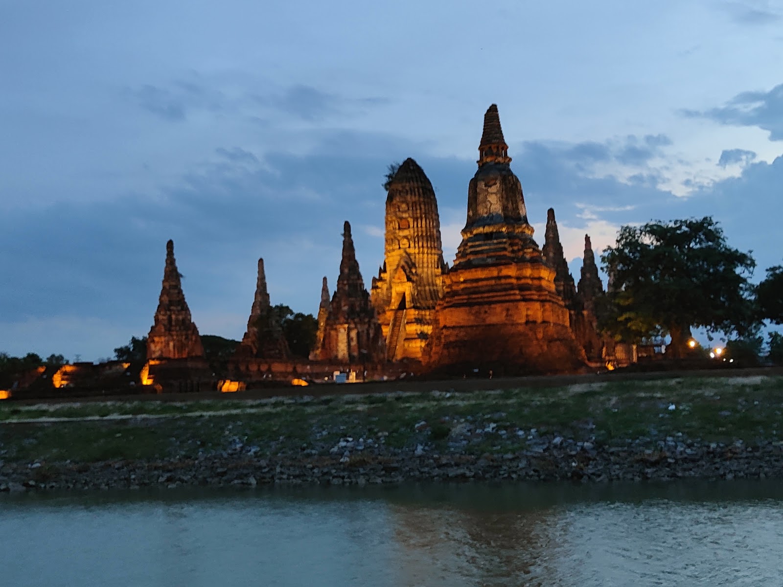 Wat Chaiwatthanaram lit up at dusk across the river with its prangs silhouetted against the sky