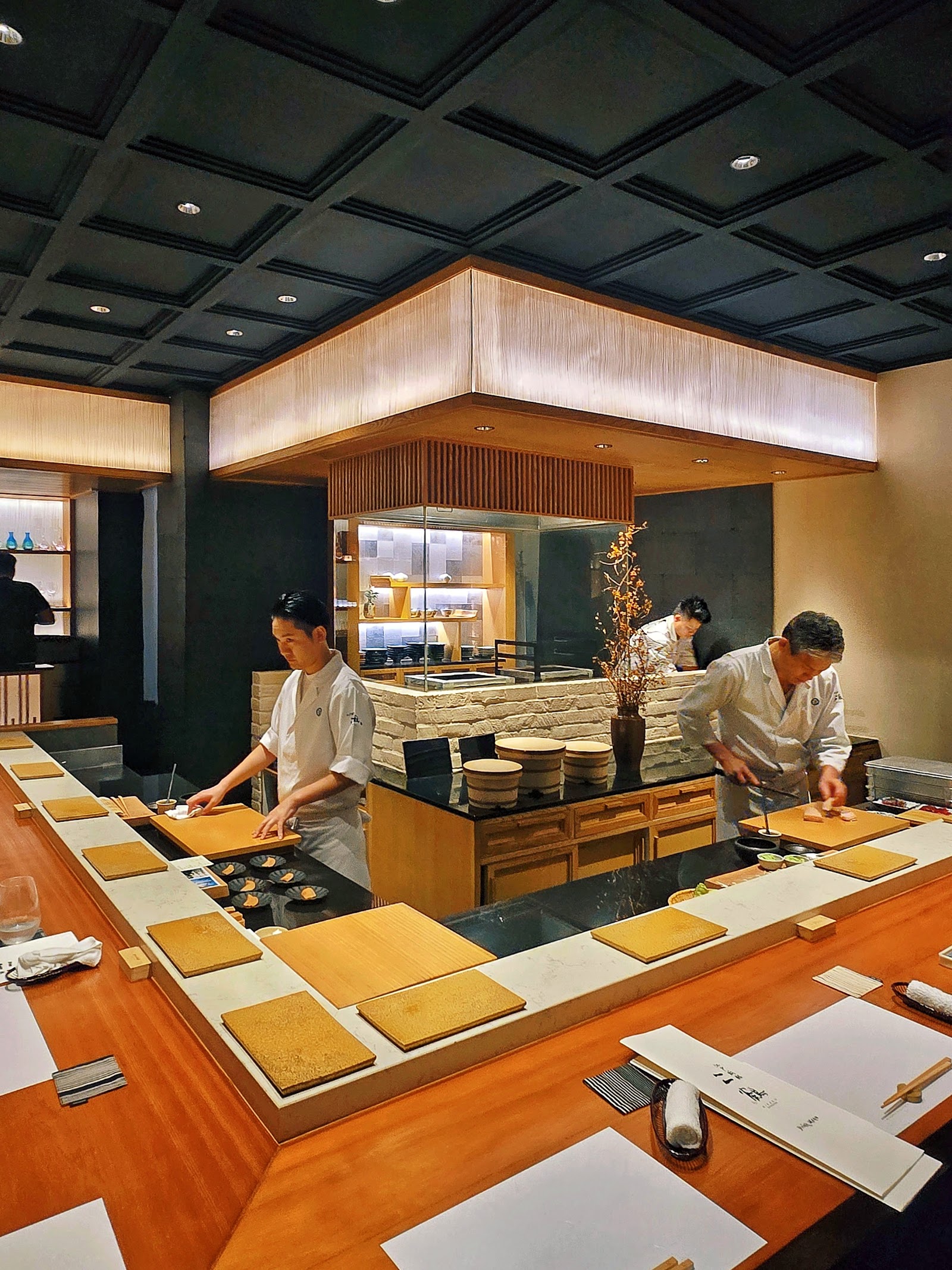The dark-ceilinged dining room at Nikaku Bangkok, with a wooden counter wrapped around the chefs' station