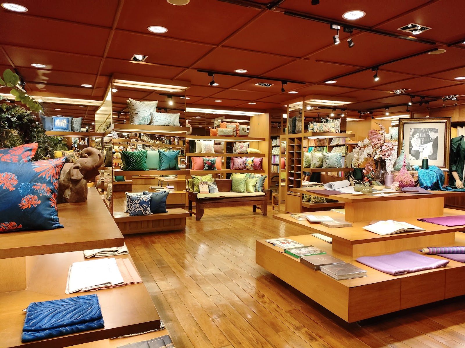 Silk cushions and scarves on wooden shelves and tables inside the Jim Thompson store on Surawong Road