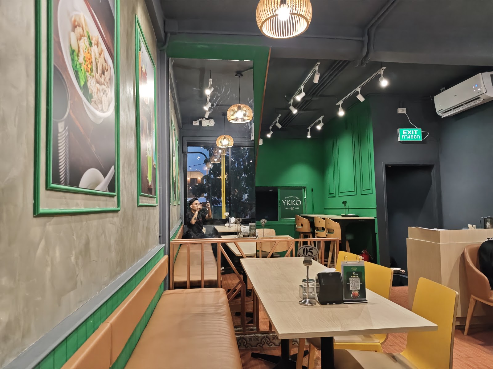 Green-painted dining room at YKKO Phra Khanong with framed noodle pictures and wooden tables
