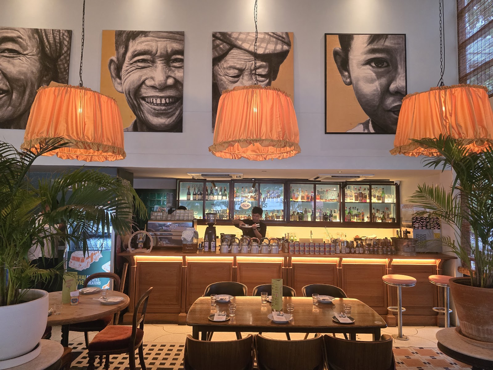 Rangoon Tea House Bangkok interior with orange pendant lamps and large portrait paintings above the bar