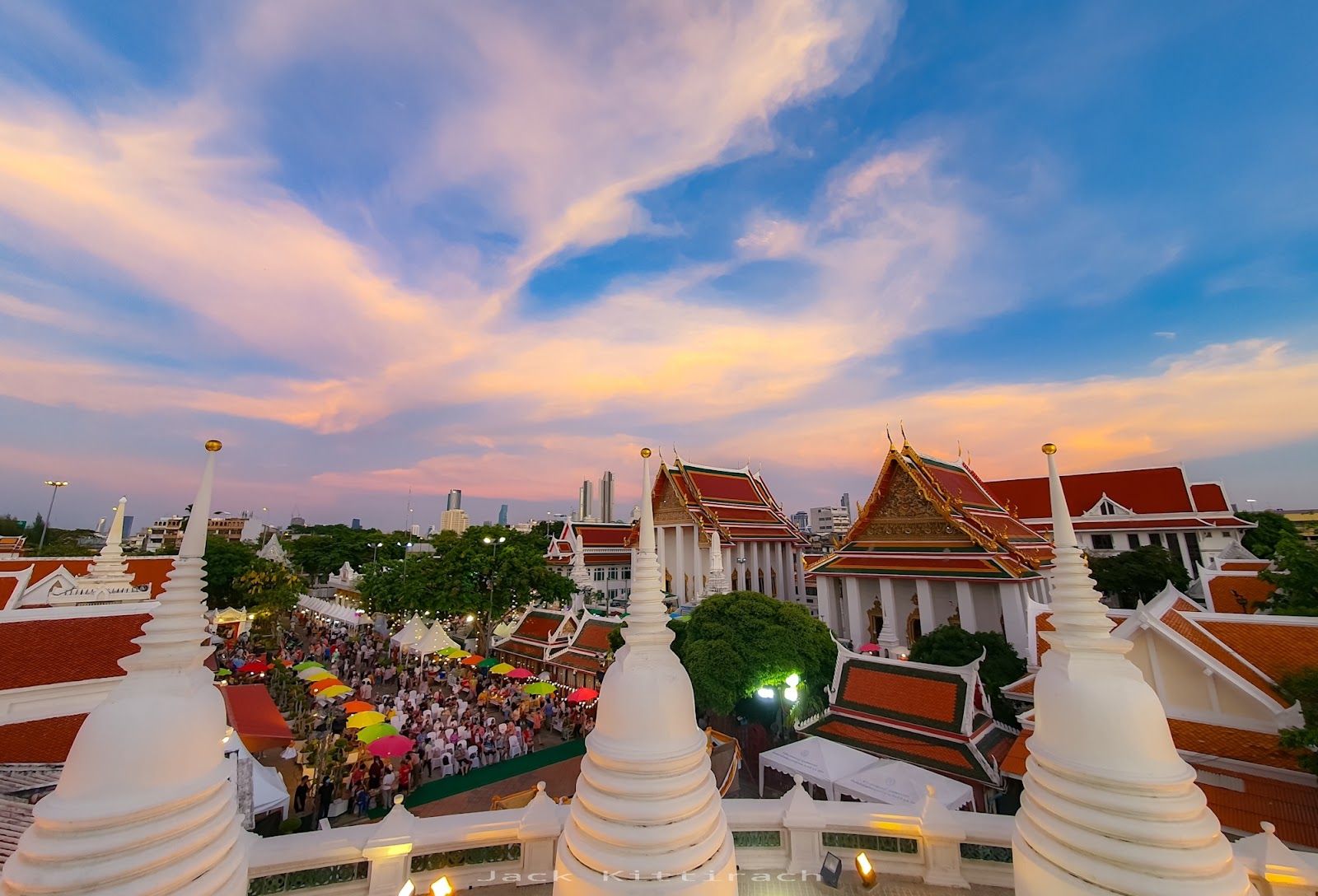 White chedis of Wat Prayurawongsawas with temple roofs and the city beyond at dusk