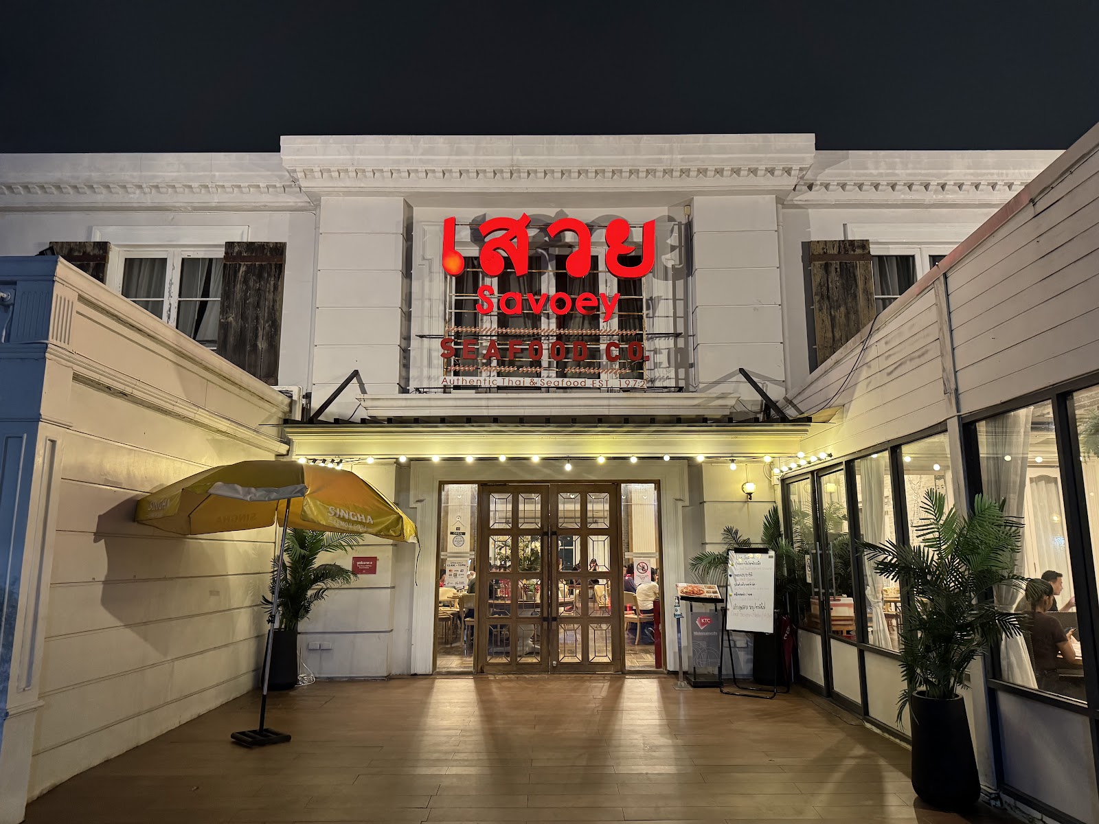 White colonial-style facade of Savoey Seafood Co. with its red Thai-script sign at dusk