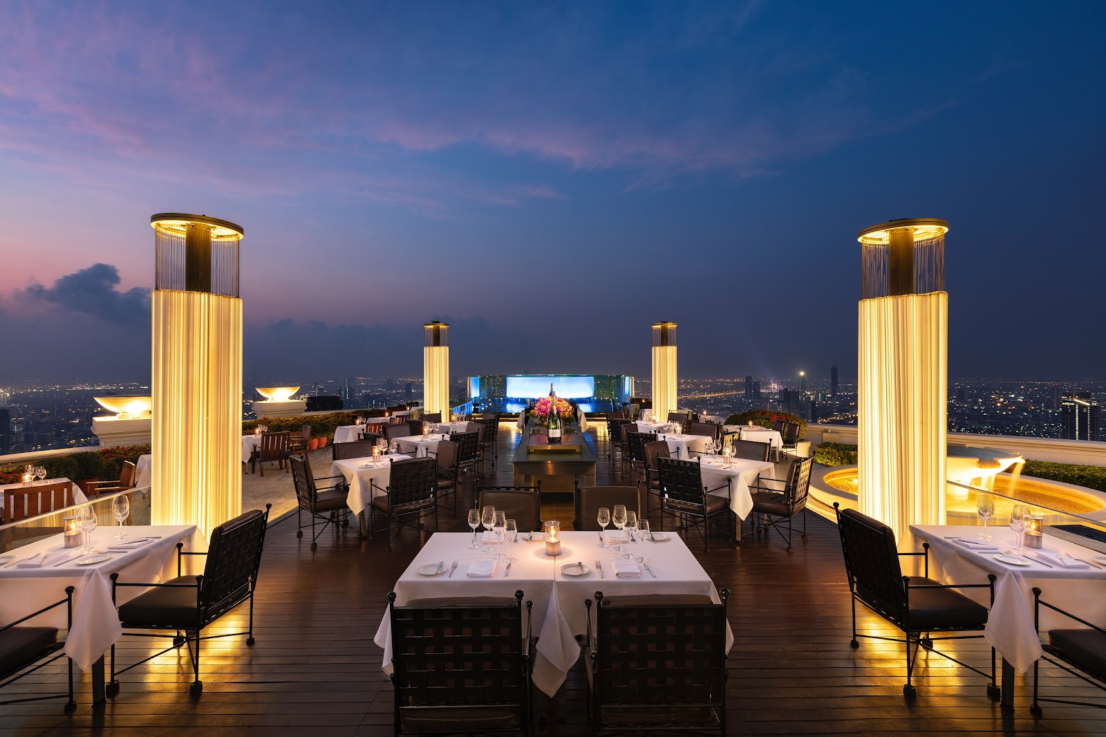 Dinner tables set between illuminated columns on an open-air terrace high above the city