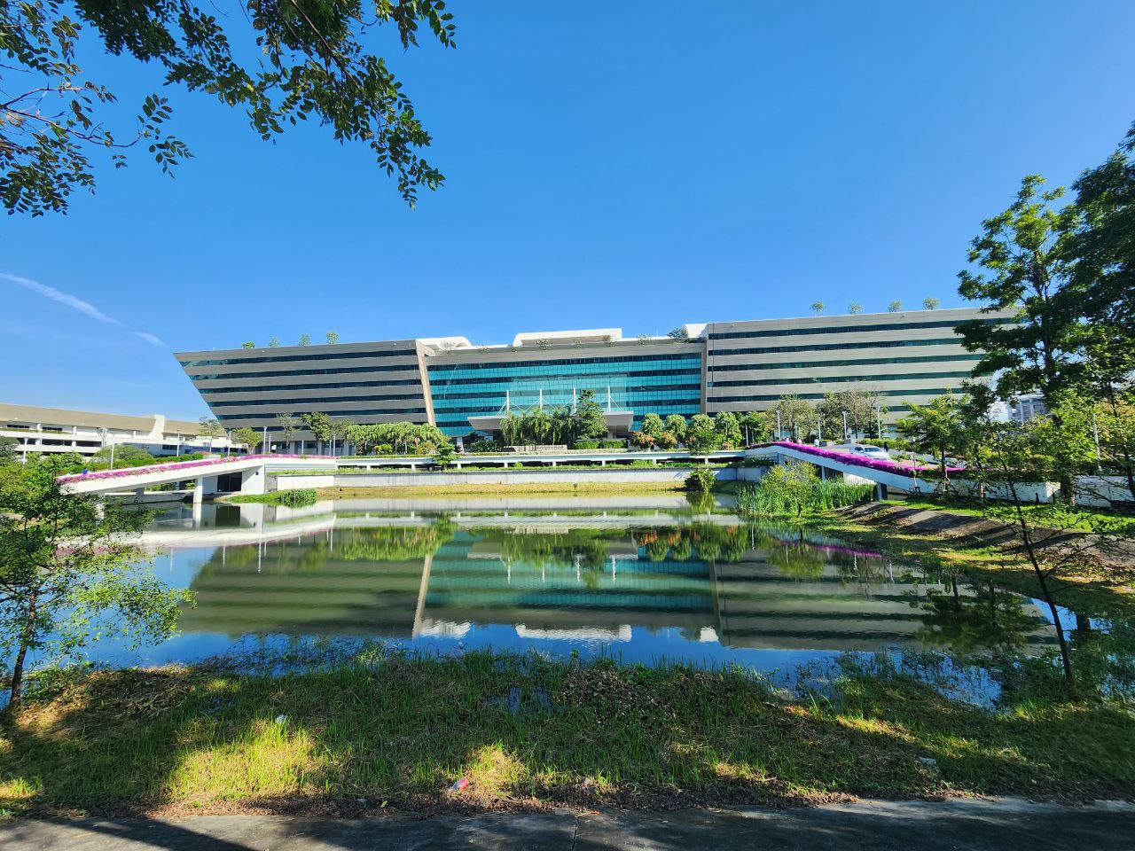The long low-rise Government Complex on Chaeng Watthana Road reflected in a pond under a blue sky