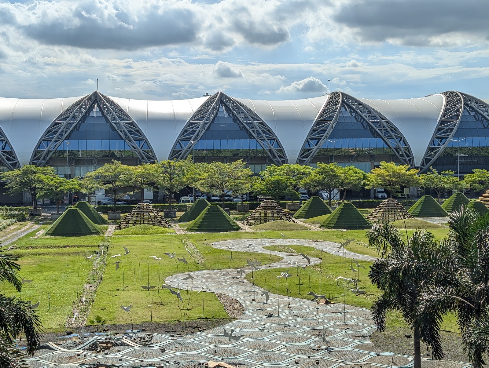 The curved glass roof of Suvarnabhumi Airport passenger terminal behind landscaped gardens