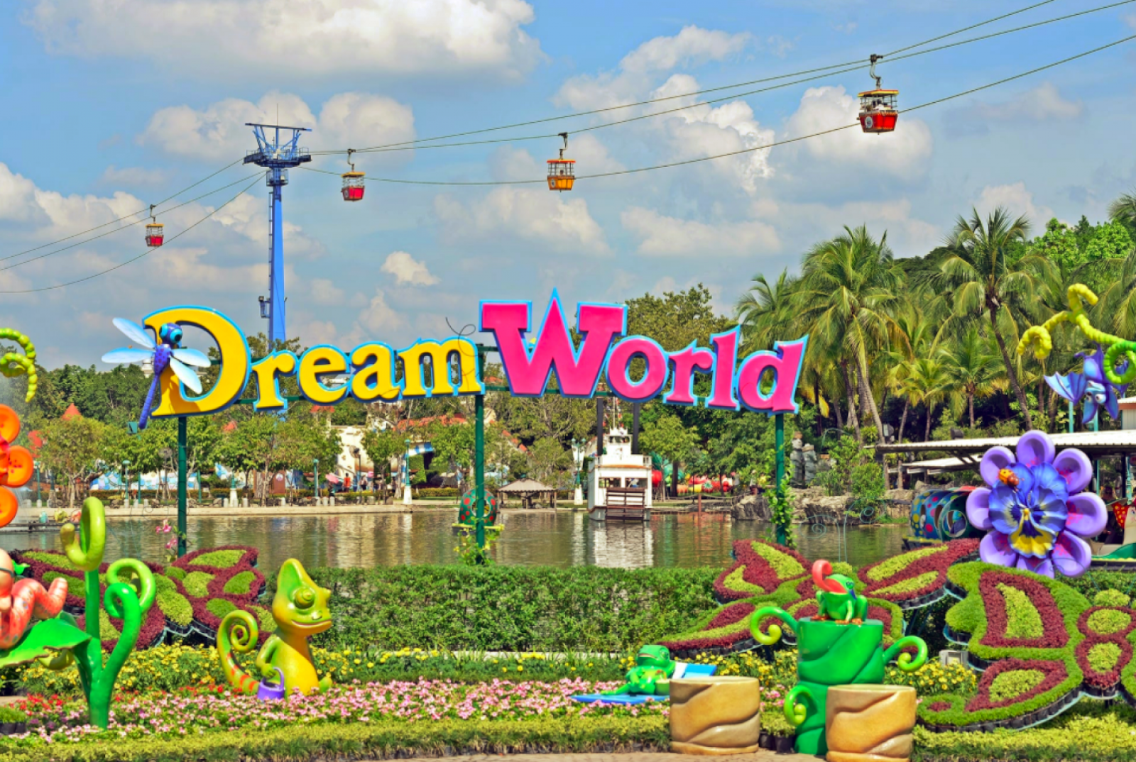 The Dream World name in large letters on a flower-planted bank, with cable cars crossing overhead